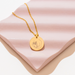 [main] A gold  pendant necklace with a gold chain featuring a mother breastfeeding her child. 