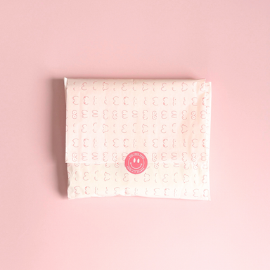 [main] Light Pink tissue paper featuring hot pink shapes of different boobs across the tissue paper to represent breastfeeding, featuring our signature Use Your Voice Smiley Face sticker in the center. 
